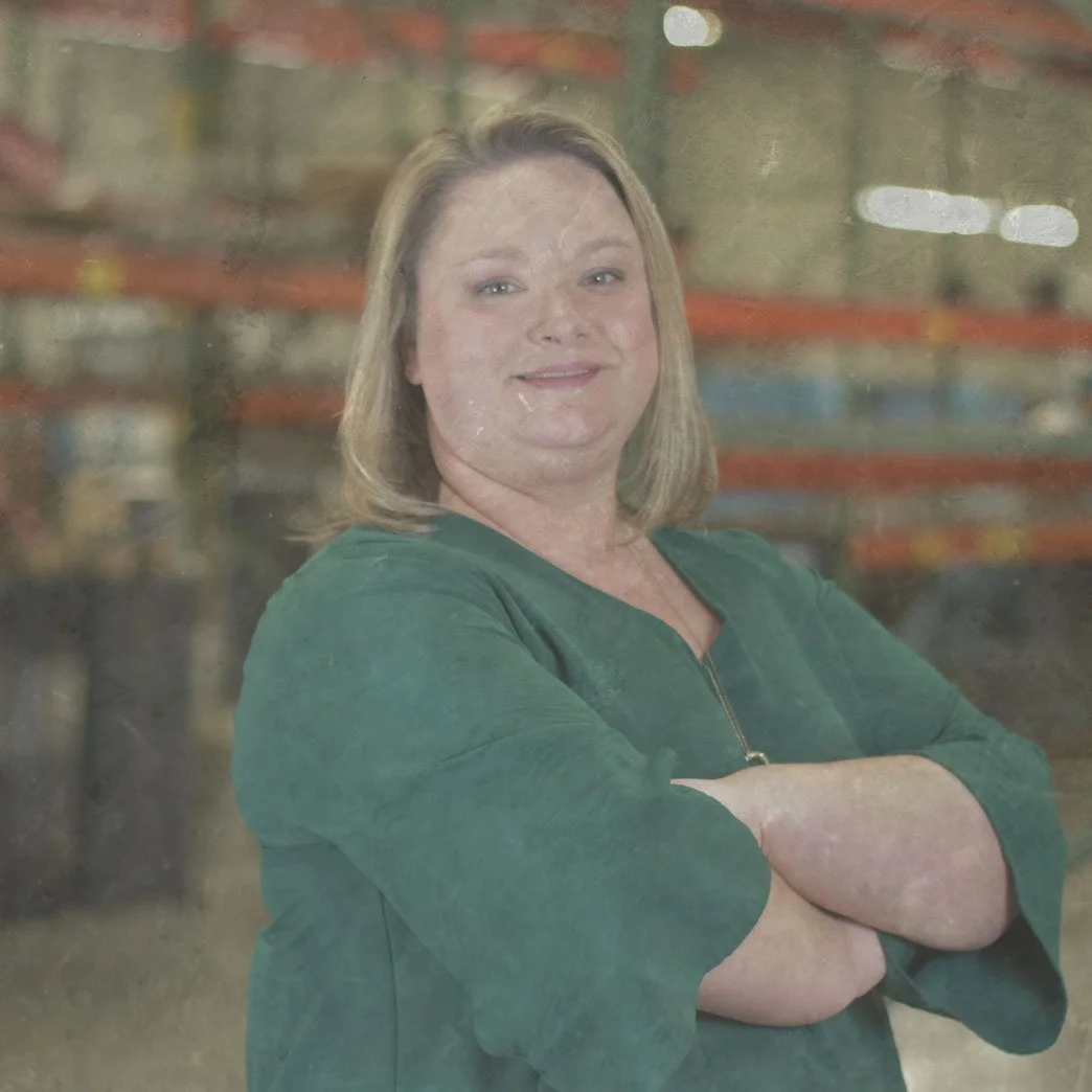Woman in green blouse standing with arms crossed in a warehouse.